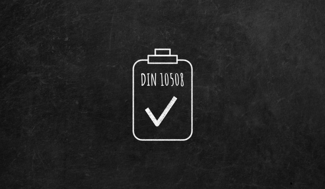 Schwarze Tafel mit einer Kreidezeichnung eines Klemmbrettes auf dem DIN 10508 steht