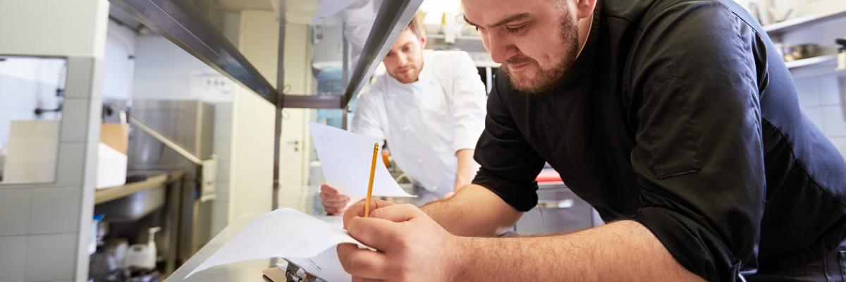 Koch in Großküche geht Liste mit Bestellungen durch.